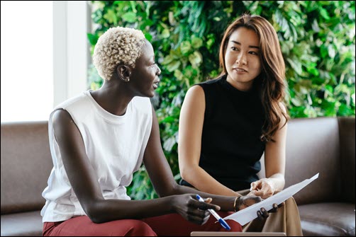 two women sitting on a couch, one is speaking and one is listening